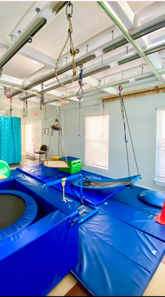 Therapy room with blue padded mats and overhead rigging equipment